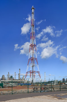 Red and white flare mast with a oil refinery on the background against a blue sky with dramatic clouds, Port of Antwerp, Belgium