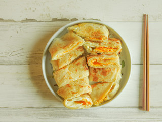 Top view of delicious Chinese omelet with cheese in white plate and bamboo chopsticks on wooden pattern background.It contains yellow egg,cheese and handmade pancake,is popular breakfast  in Taiwan.