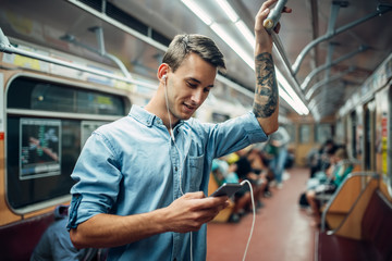 Young man using phone in metro, addicted people - obrazy, fototapety, plakaty