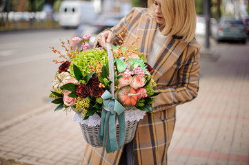 Blonde woman holding a wicker basket of autumn flowers against the city