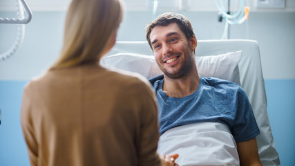 In the Hospital, Man Recovering from Illness Lying in Bed, Loving Wife Visits Him. He is Smiling...