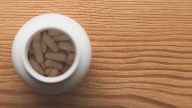 A white pill bottle containing opioid drugs on a wooden table top. This image can be used to represent healthcare or medicine. 