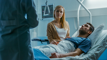 In the Hospital, Patient Lying in Bed, his Wife Sitting Beside the Sick Man Listens to Doctor's Explanations. Love and Care Concept.