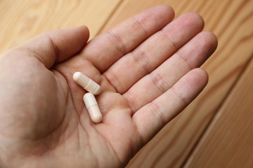 A human hand holding two white opioid pills.  This image can be used to represent medication or a doctor's prescription. 