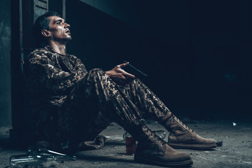 Soldier Is Sitting In War Shelter With Shotgun.