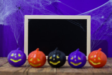 Halloween background concept. Blackboard with decor pumpkins, cobweb on wooden table and purple backdrop