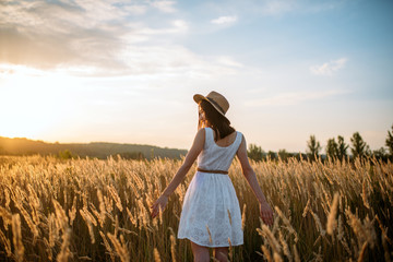 Woman in dress walking in wheat field on sunset