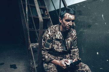 Fototapeta na wymiar Soldier Is Sitting In War Shelter With Shotgun.