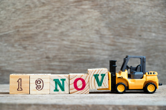 Toy forklift hold block V to complete word 19nov on wood background (Concept for calendar date 19 in month November)