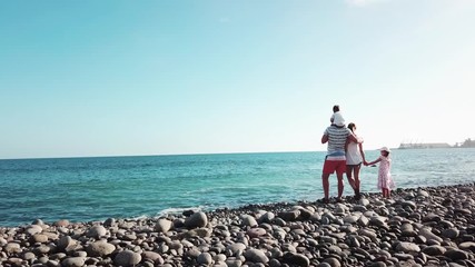 Beautiful family of four is standing on a coastline and staring the ocean and clear blue sky. Summer travel vacation for family in Gran Canaria.