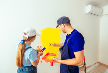 Couple painting wall at home in yellow color