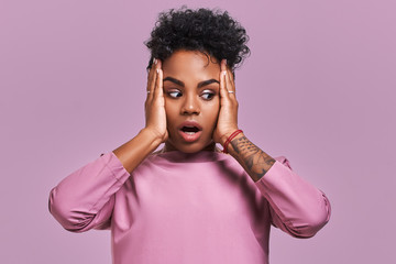 Fototapeta na wymiar Gorgeous beautiful female with dark skin, opens mouth wide and expresses surprisement, receives shocking news, isolated on yellow studio background with lavender wall