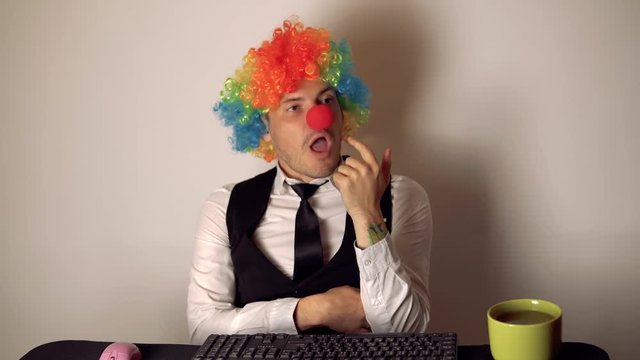 Office worker in the form of a clown working in the office at the computer. The concept of a clown at work, slacker