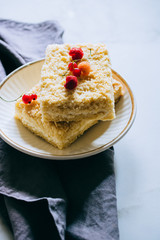 Pieces of cottage cheese cake with a crumble decorated with raspberries and red currants on a white plate