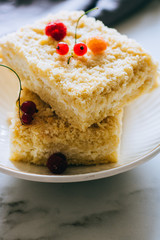 Pieces of cottage cheese cake with a crumble decorated with raspberries and red currants on a white plate