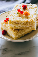 Pieces of cottage cheese cake with a crumble decorated with raspberries and red currants on a white plate