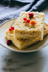 Pieces of cottage cheese cake with a crumble decorated with raspberries and red currants on a white plate