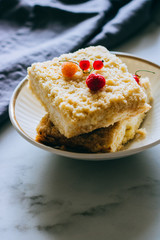 Pieces of cottage cheese cake with a crumble decorated with raspberries and red currants on a white plate