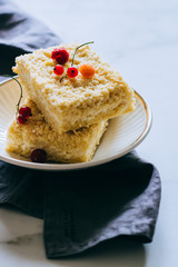 Pieces of cottage cheese cake with a crumble decorated with raspberries and red currants on a white plate
