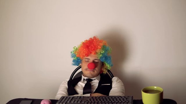 Office worker in the form of a clown working in the office at the computer. The concept of a clown at work, slacker