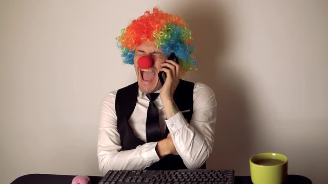 Office worker in the form of a clown working in the office at the computer. The concept of a clown at work, slacker