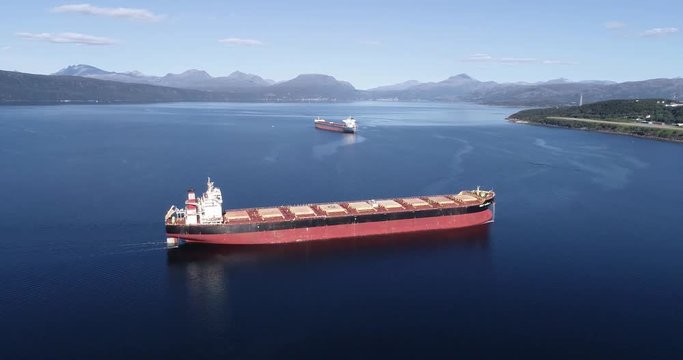 Aerial footage of a cargo ship on the open sea with other ship and mountains in the background, Narvik, Norway