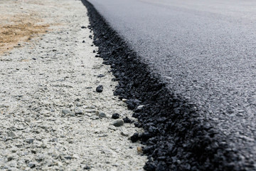 newly laid black bitumen asphalt with a high edge to the gravel