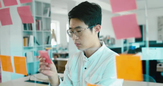 Asian Chinese employee looking onto a glass wall with sticky notes, framework for managing work, scrum methodology. 4K UHD 60 FPS SLOW MOTION