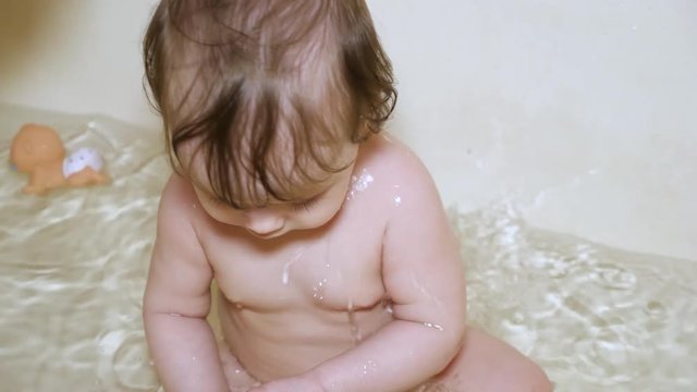 little baby is bathing in bathroom and playing, mother is pouring water on the baby
