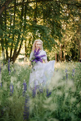 Fototapeta na wymiar Beautiful young girl in the flowers of lupine. Girl with blonde hair in a long dress with a bouquet of flowers