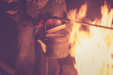 Hand of man taking the kettle, wich heated on a fire at night outdoor, toned photo