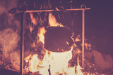 The kettle is heated on a fire at night outdoor, toned photo