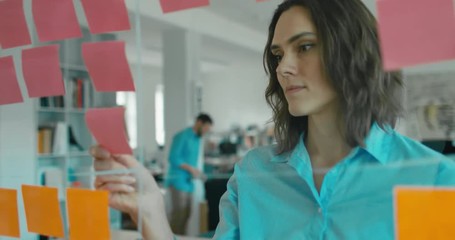 Caucasian female worker standing near glass wall with sticky notes, framework for managing work, scrum methodology. 4K UHD 60 FPS SLOW MOTION