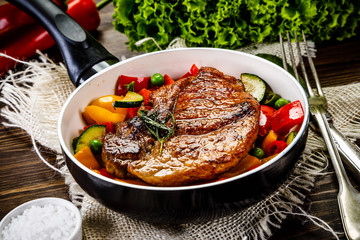 Grilled steak with vegetables in pan on wooden table
