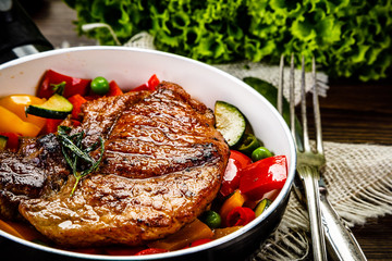 Grilled steak with vegetables in pan on wooden table