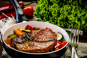 Grilled steak with vegetables in pan on wooden table