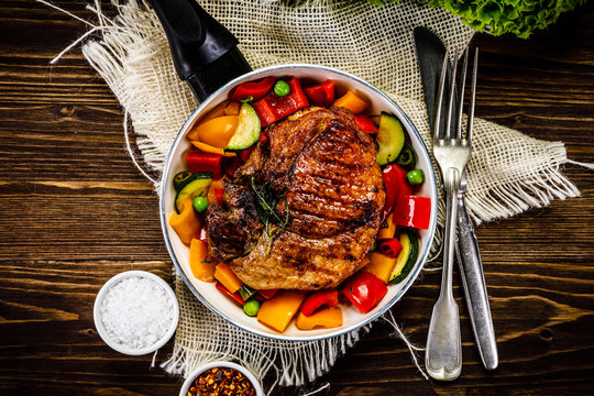 Grilled steak with vegetables in pan on wooden table