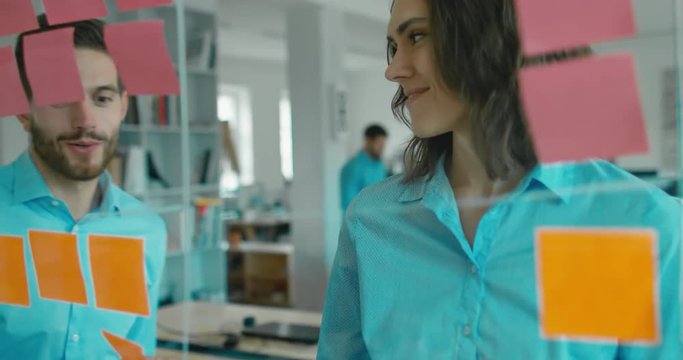 Caucasian colleagues standing near glass wall with sticky notes, framework for managing work, scrum methodology. 4K UHD 60 FPS SLOW MOTION