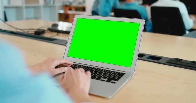 Young Caucasian woman sitting in the office, working on a laptop, green screen chroma key. 4K UHD 60 FPS SLO MO