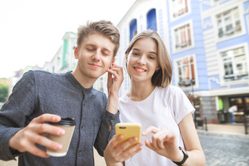 Street portrait of a happy young couple who listens to music from one headphone. girl smiles, the guy listens to music with her eyes closed. Beautiful couple walks around the town.
