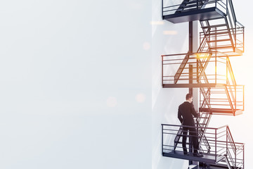 Man standing on fire escape stairs, white wall