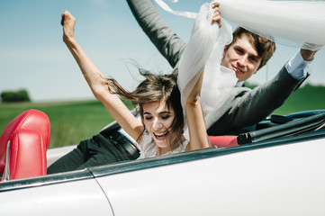 Happy bride and groom, newlywed wedding couple is driving a convertible retro car with balloons on...