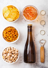 Glass and bottle of craft lager beer with snack and opener on stone kitchen table background....