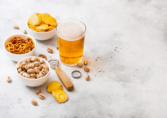 Glass of craft lager beer with snack and opener on stone kitchen table background. Pretzel and crisps and pistachio in white ceramic bowl. Space for text