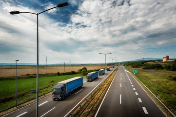 Caravan or convoy of blue lorry trucks in line on a country highway