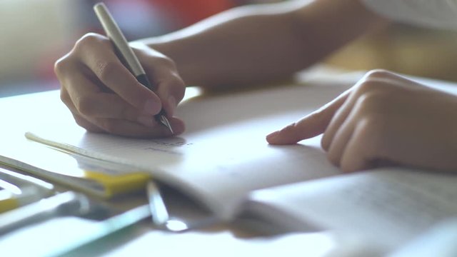 Close-up shot of boy's hand writing on book while doing homework at home