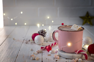 Enamel cup of hot cocoa with mini marshmallows and candy canes with beautiful Christmas lights of...