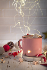 Enamel cup of hot cocoa with mini marshmallows and candy canes with beautiful Christmas lights of...