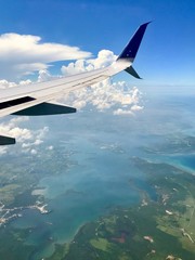 Fototapeta premium Freedom: Aerial view from above the clouds with a wing of an airplane in the sky over Cuba approaching the city of Havana (scenic journey over the ocean with beautiful view and cloudscape)