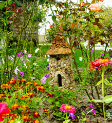 A small stone house for gnomes in a flower bed among the flowers. fairytale house